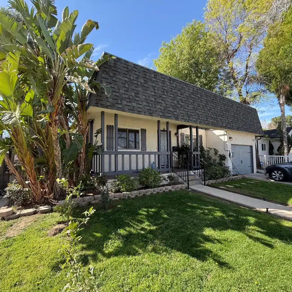 Encino home with new asphalt shingle roof and front porch, lush landscaping under blue sky, roofing contractor Encino by Roofing Angels in Encino, CA